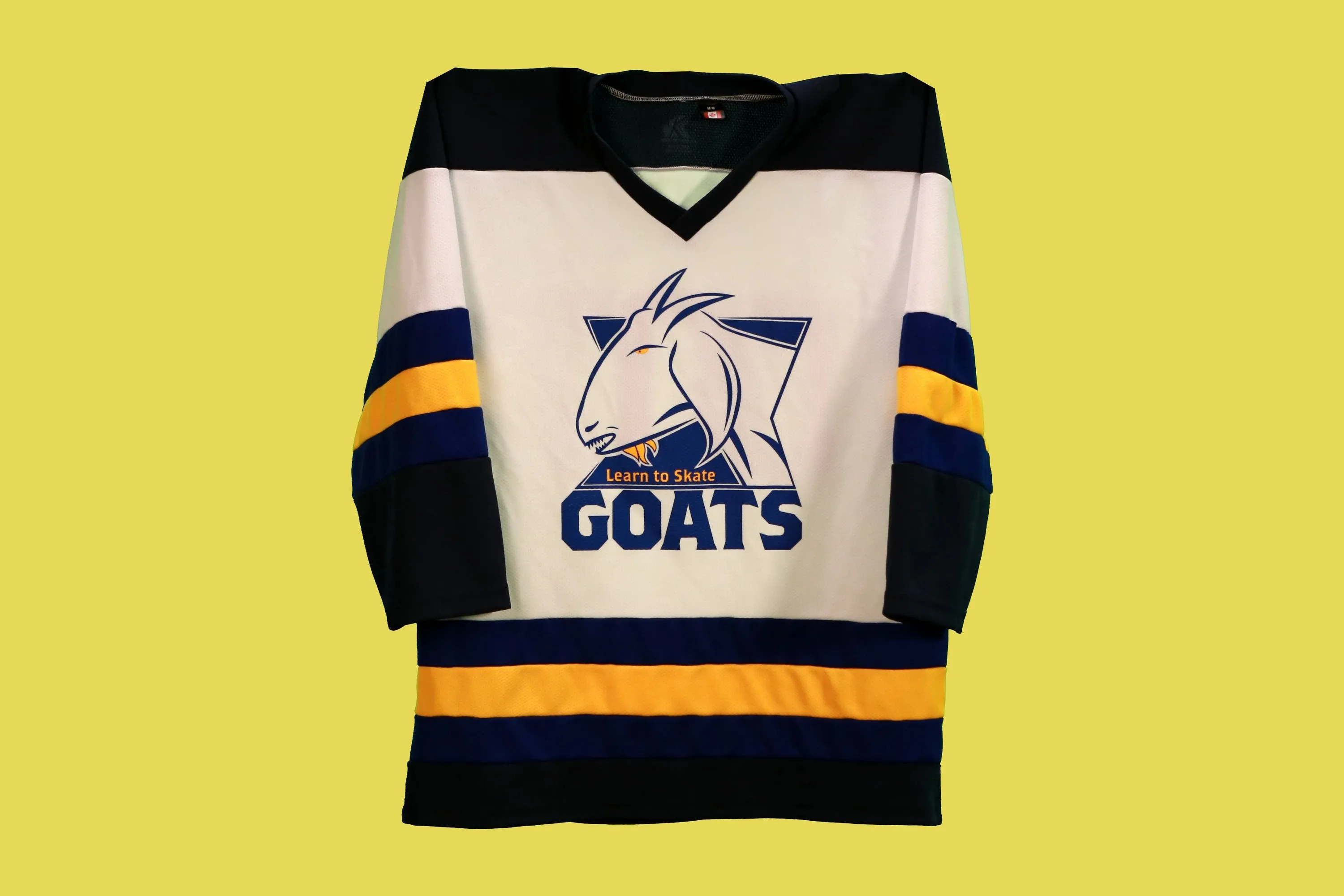 White Goats hockey jersey with navy and gold stripes and the “Learn to Skate Goats” logo on the chest